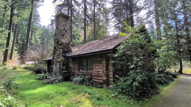 Historic log cabin with moss-covered cracks, a towering stone chimney, gravel pathway, and surrounding evergreens, preserving Oregon&rsquo;s pioneer heritage in a serene woodland setting.
