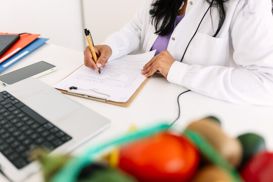 Female dietitian writing patient notes during remote consultation. Healthcare specialist reviewing nutrition assessment documents. Nutrition and healthcare concept.
