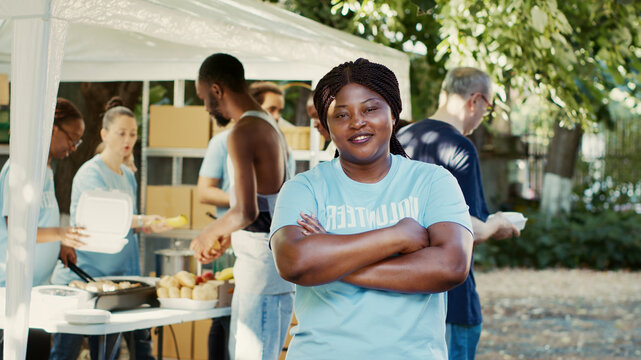 Happy black woman with crossed arms and blue t-shirt looking at camera, image shows African American volunteer who is prepared to help needy.