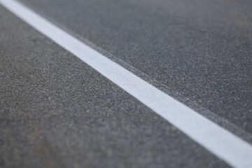 Fototapeta premium Ligne blanche sur la route, gros plan d'une photo à faible profondeur de champ. Texture de route asphaltée avec ligne blanche. Fond et texture abstraits pour le design.