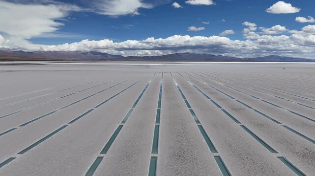 Cinematic low angle aerial footage of geometric water trenches for mineral extraction in the vast white salt flats of Salinas Grandes, Salta, Argentina.