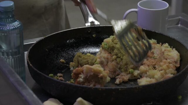 cooking of potato-based mixture with vegetables in a pan using a spatula. the image shows a homemade cooking process with ingredients being mixed and prepared in a kitchen