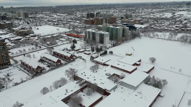 Aerial over Mississauga, Ontario, Canada on a cold winter morning after snowfall March 2023. Cooksville area. Snow covered rooftops and school.