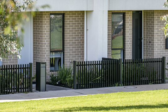 Street view of modern townhouses featuring aluminium picket fencing, a letterbox post, windows and individual front entry doors in a new suburban residential estate, Melbourne, Australia