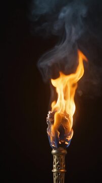Carved antique golden torch with an intense orange fire flame and wispy white smoke rising on a black background.