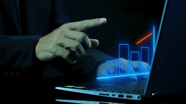 Businessman working with laptop computer showing chart and graph icons on virtual hologram digital screen interface in 4K Ultra HD footage.
