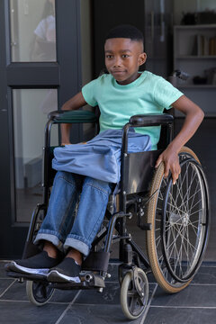 African American schoolboy sitting in manual wheelchair at entrance gripping wheel, backpack on lap
