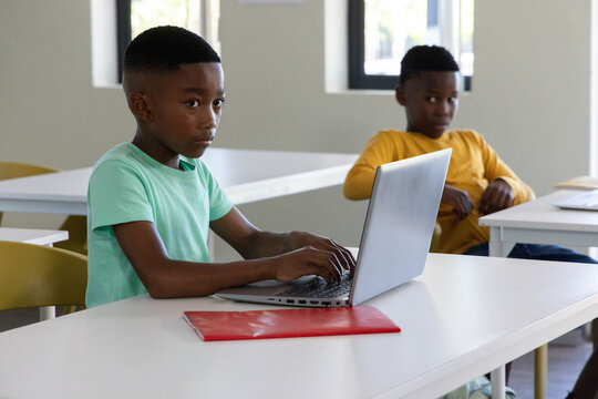 African American schoolboys typing on silver laptop, red folder on table in classroom, copy space