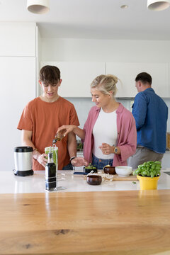 Family parents and teenage son preparing smoothie at kitchen island, pouring oil into blender cup