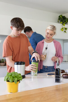 Family with teenage son preparing food while teen securing personal blender cup at kitchen island