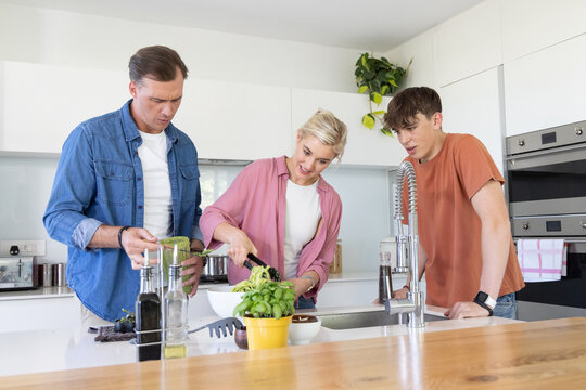 Parents and teenage son preparing salad at kitchen island, mother in pink shirt using tongs