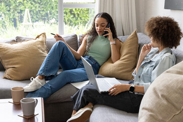 Obraz premium African American women reclining and working on laptop while speaking on smartphone in living room