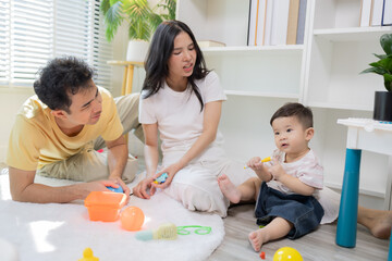 Fototapeta premium Warm sunlight streams through blinds. Family of three smiles softly in cozy room. Mother holds infant close, father looks lovingly on. Green plant adds freshness to minimalist shelves 
