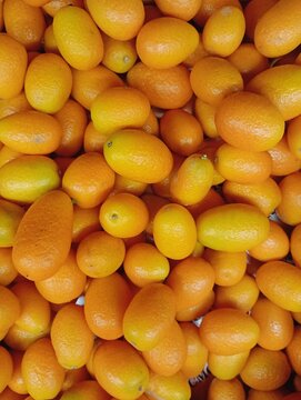 Textured background of a dense pile of fresh ripe orange kumquat fruits. High-quality exotic citrus photography ideal for healthy food blogs, grocery store promotions, organic juice packaging designs,