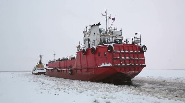 Winter River Navigation: Tugboat Pulling Cargo Barge Through Ice. Russian Tugboat Escorting Barge Along an Icy Waterway