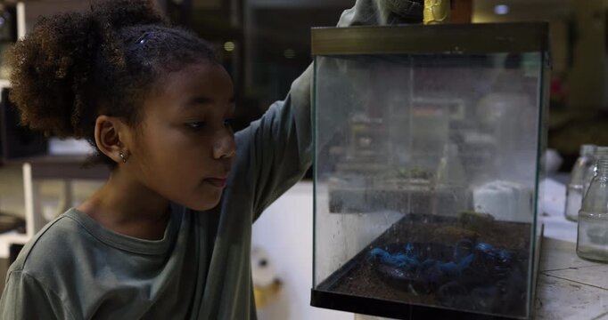 Young girl fascinated by a UV glowing scorpion inside a terrarium during a hands-on science education activity. The image highlights curiosity, wildlife exploration, STEM learning