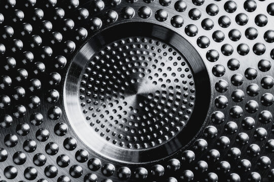 A close-up view of a metallic surface with raised studs and a central perforated circular region, showcasing industrial texture and detailed engineering design.