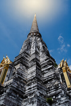Low angle view of ancient weathered Thai pagoda with golden spire under blue sky.