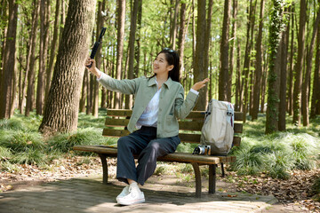 Fototapeta premium Young woman taking selfie on bench in forest park