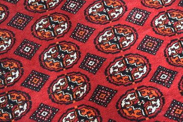 Naklejka premium Close up of a traditional Turkmen handmade wool carpet with authentic red and black geometric patterns. Geometric tribal ornament texture on an oriental nomadic rug, central asian textile art. 