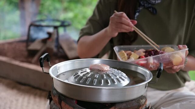 A woman cooking and eating Moo Kata, Thai barbecue grill pork