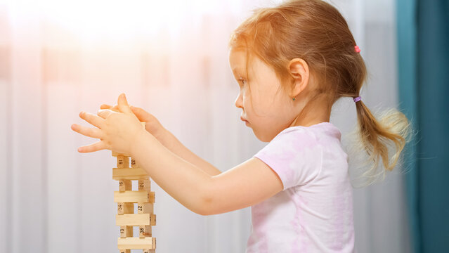 Young girl carefully balancing wooden blocks, building a tall tower while focusing intently, developing fine motor skills and problem solving abilities during indoor play