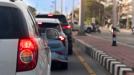Tight rear view focusing on a white car illuminated red tail light during a traffic jam. A blue car and other commuter vehicles stand queueing on the busy urban roadside lane. Driving on asphalt road. © thongchainak
