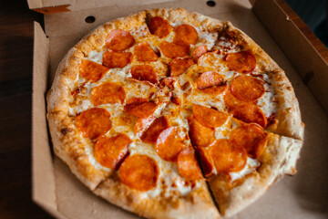 A freshly baked pepperoni pizza in a cardboard box. The pizza has a golden crust and is topped with melted cheese and slices of pepperoni.