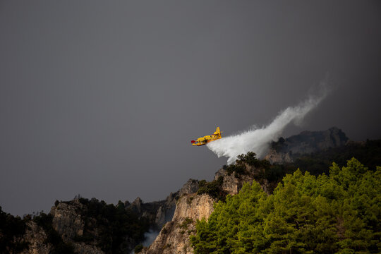 POSITANO, ITALY - OCTOBER 01, 2018: Yellow Canadair firefighter plane releasing a water over a burning mountain area. Civil defense crews use aerial tactical maneuvers to extinguish a forest fire.