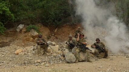 Obraz premium A military special forces team regroups amidst smoke in a rugged, rocky terrain during a tactical operation, showcasing unit cohesion and combat readiness.