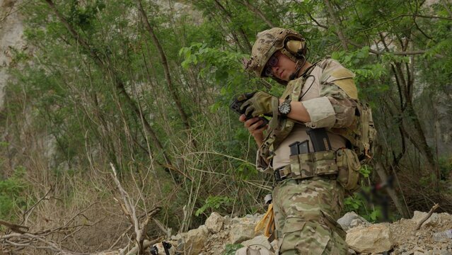A special forces soldier in a rugged forest operates a smartphone for tactical navigation and mission coordination, demonstrating modern battlefield technology.