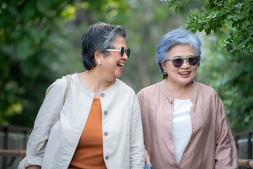 Fototapeta premium Cheerful senior women carrying shopping bags while walking through a green urban walkway