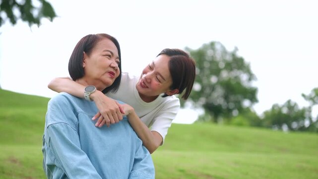 A smiling Asian daughter lovingly embraces her senior mother from behind in a green park. A heartwarming portrait capturing family love, care, and strong generational bond.
