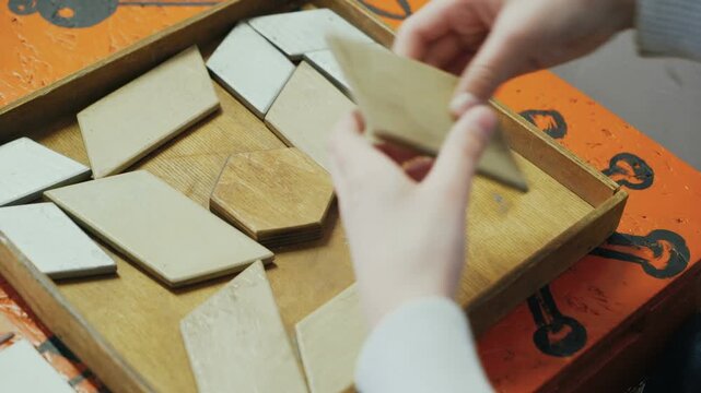 Child arranging wooden geometric shapes in a pattern puzzle on an orange table, developing fine motor skills and problem-solving abilities.