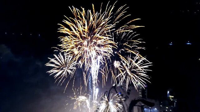Aerial view of colorful fireworks exploding over coastal city at night with sparkling light reflections.