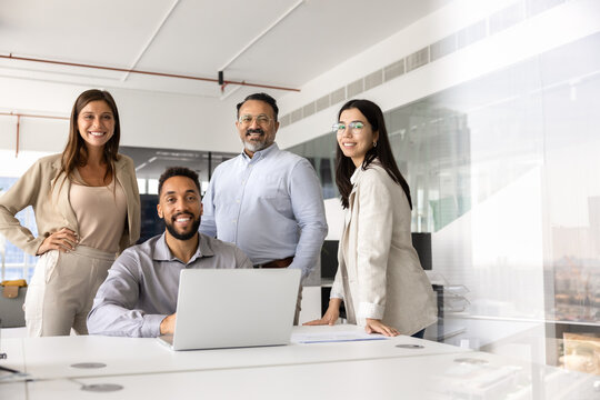 Group of diverse, young and mature colleagues posing together in modern office interior, smiling, looking at camera, representing successful teamwork, collaboration and professional unity in workspace