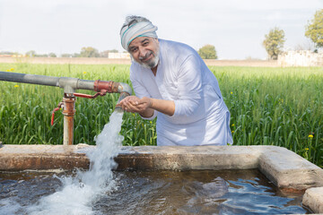 Happy Indian farmer drinking fresh water from tube well irrigation pipe in agricultural field, rural life, farming, groundwater, crop irrigation, water supply, and agriculture in India © GAJENDRRA BHATI 