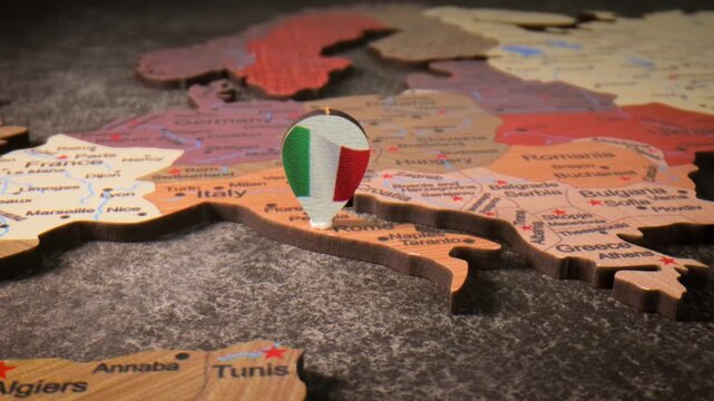 A close up view of italy on a wooden world map with italian flag pin in slow motion, europe on world map.