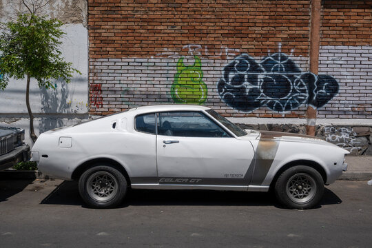 Guadalajara, Mexico - May 9 2026: A vintage white Toyota Celica GT car parked on a Guadalajara street. Graffiti on brick wall adds urban character.