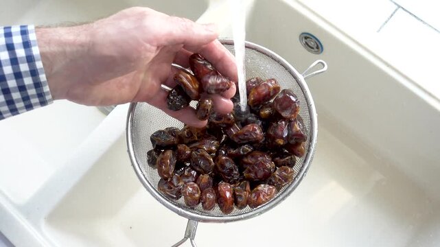 Male hands wash dried dates in a mesh strainer under running water in a kitchen sink. Concept of healthy eating and using natural sweeteners. Top view. Ideal for nutrition, vegan diet, cooking content