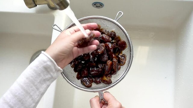 Female hands wash dried dates in a mesh strainer under running water in a kitchen sink. Concept of healthy eating and using natural sweeteners. Ideal for nutrition, vegan diet, and cooking content