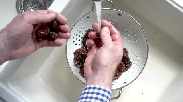 Male hands wash dried dates in a mesh strainer under running water in a kitchen sink. Concept of healthy eating and using natural sweeteners. Top view. Ideal for nutrition, vegan diet, cooking content