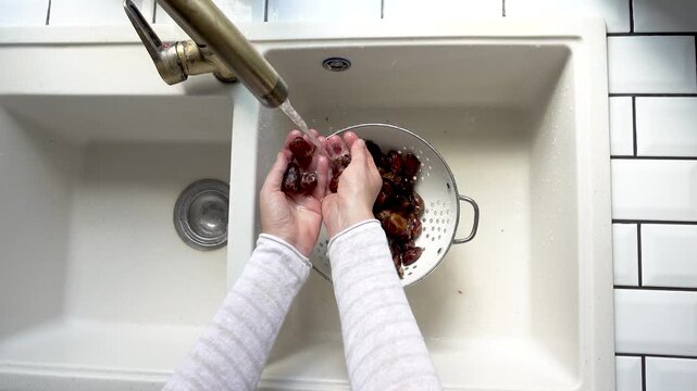 Female hands wash dried dates in a mesh strainer under running water in a kitchen sink. Concept of healthy eating and using natural sweeteners. Ideal for nutrition, vegan diet, and cooking content