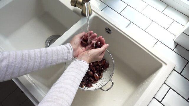 Female hands wash dried dates in a mesh strainer under running water in a kitchen sink. Concept of healthy eating and using natural sweeteners. Ideal for nutrition, vegan diet, and cooking content