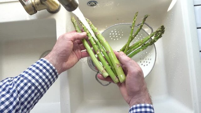 Male hands wash asparagus under running water over a metal colander in a kitchen sink. Concept of healthy eating and using natural sweeteners. Ideal for nutrition, vegan diet, and cooking content