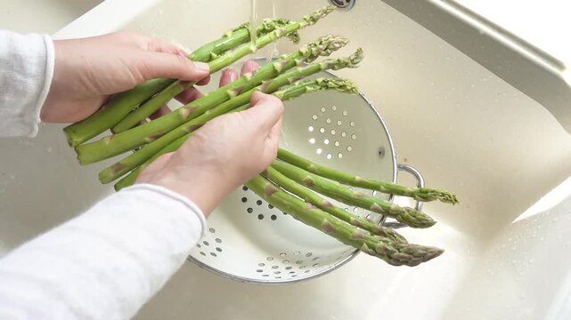 Female hands wash asparagus under running water over a metal colander in a kitchen sink. Concept of healthy eating and using natural sweeteners. Ideal for nutrition, vegan diet, and cooking content
