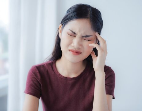 Young Asian Woman Experiencing Headache and Facial Pain Indoors.