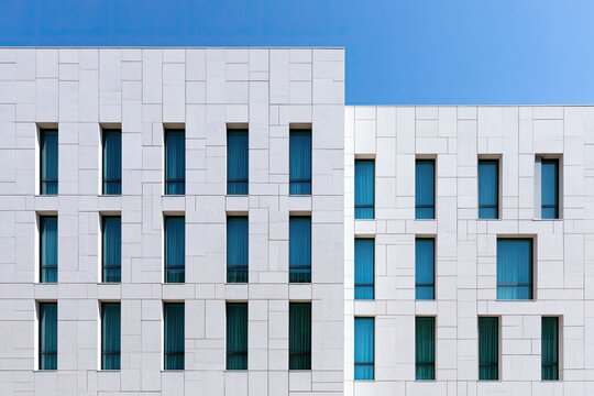 Modern white residential building facade with narrow windows under clear blue sky