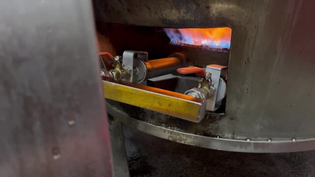 Close-up view of industrial gas burner flame providing heat to a cooking kettle during food production. Energy source used in food manufacturing and industrial cooking processes.
