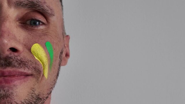 A fan paints green and yellow stripes on their face, representing the colors of their national team's flag, Brazil or Jamaica. This shows support for the national football team and country